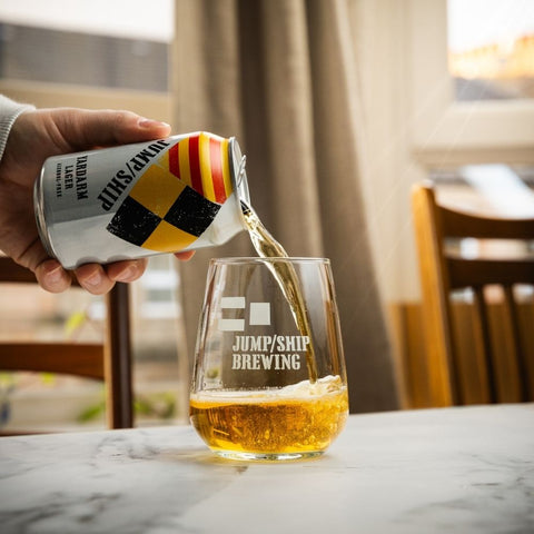 Hand pouring a can of Yardarm Lager from Jump Ship brewing in a home setting