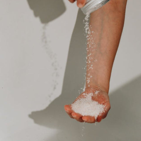 A person emptying an aluminium tin of bath salts directly on a hand palm on the white bath tub background.