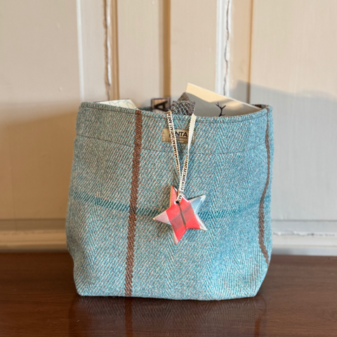 Blue plaid handcrafted Scottish gift bag with a pink star-shaped Christmas decoration on a wooden surface