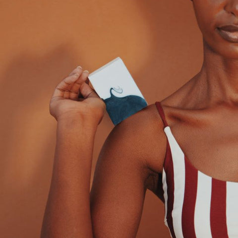 A women in a white and red striped top, on the orange background holding a bar of soap on her arm.