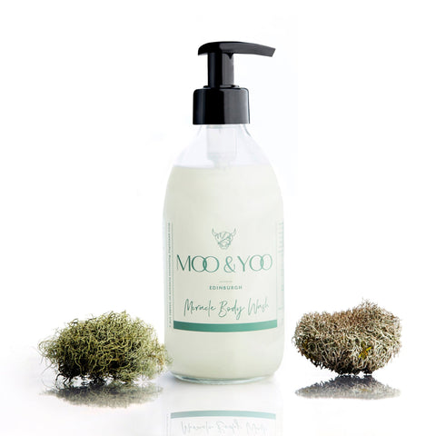 Glass bottle of Moo and Yoo Body Wash with a pump on a white background with a sprig of moss to each side.