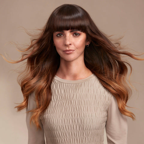 Female model with a wavy bob and brunette hair. She has super shiny hair and has used Moo & Yoo Miracle Conditioner and Volumising Spray Mist so she has  lots of volume. She is looking at the camera from a side angle and is wearing a neutral coloured shirt.