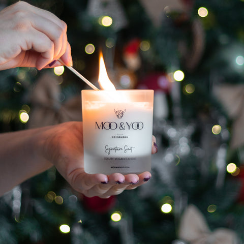 Person lighting a MOO & YOO candle with a Christmas tree in the background