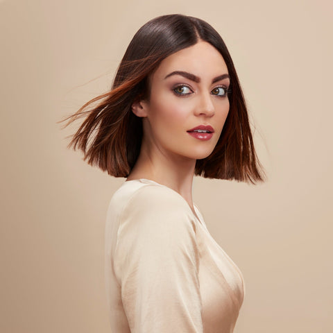Woman with a stylish sleek brunette bob haircut flowing in the wind against a beige background