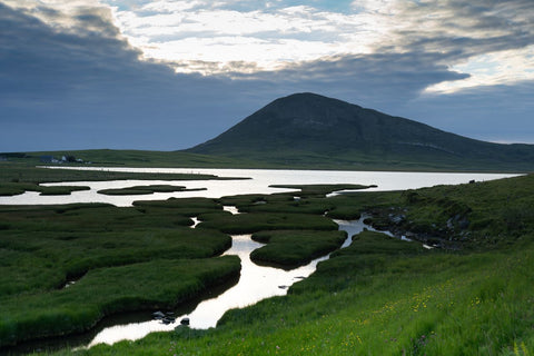 Landscape with a river flowing through green fields towards a mountain under a cloudy sky. Northton, Isle of Harris, Scotland, where the croft of A.S Apothecary is