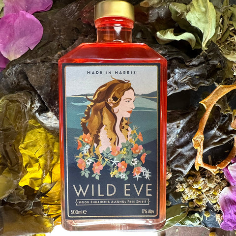 A 500ml bottle of Wild Eve alcohol-free spirit, with a label featuring an illustration of a woman surrounded by floral elements. The bottle is placed against a backdrop of natural elements, including various plants and flowers.